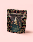 A decorative tea pouch labeled "Persephone's Potion: Pomegranate & Jasmine Green Tea" features floral patterns, an illustration of a woman among roses, and highlights jasmine green tea notes on a pale pink background.