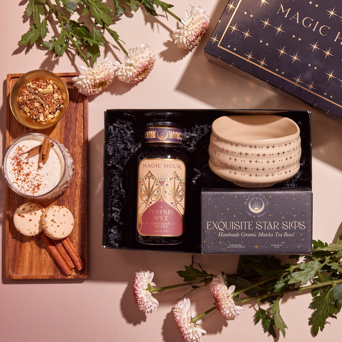 Introducing the Pumpkin Lovers Tea & Accessory Gift Set: a charming collection featuring a pumpkin spice tea jar and a star-patterned ceremonial tea bowl. This delightful ensemble includes cinnamon sticks and spice-dusted cookies, with cream and herbs beautifully arranged. The set is completed with flowers and a starry box, making it the perfect gift for any occasion.