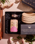 The Pumpkin Lovers Tea & Accessory Gift Set includes a jar labeled "Magic Hour," a box of "Exquisite Star Sips," a luxurious ceremonial tea bowl, and a cup of pumpkin spice tea. It comes paired with macarons and cinnamon sticks, all beautifully arranged on a wooden tray with decorative flowers elegantly surrounding these delightful items.