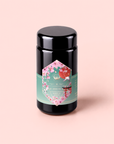 A canister of Queen of Kyoto green tea, featuring a pink floral label with a green band, is displayed against a light pink background. The label highlights its Sencha Green Tea blend, inspired by the lively spirit of the Cherry Blossom Festival.