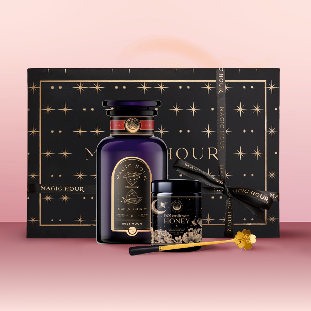 The Tea & Honey Gift Set features a dark bottle, Wildflower Honey with gold honey dipper, and a large black box with gold stars and "Magic Hour" on pink—an elegant choice for your morning ritual.