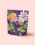 A purple stand-up pouch with colorful passion fruit, flowers, and green leaves on pink hints at "Romance in Ravello"—a Chocolate-Passionfruit-Rose-Cream White Tea blend inspired by the Amalfi Coast.