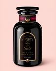 A black apothecary-style jar labeled “Magic Hour Ruby Moon™ : Hibiscus Elderberry Tea” with gold celestial designs stands on a light pink background. The label features “Time for Infinity” and notes that it is a “Ceremonial tea made with love.” This exquisite jar contains a healing herbal blend—a luxurious, caffeine-free hibiscus elderberry tea that’s as enchanting as its celestial motif.
