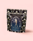 A decorative bag of Skadi The Sovereign: Winter Berry Puerh tea features floral patterns and a dancing woman beneath an arch on a black background, symbolizing winter resilience.