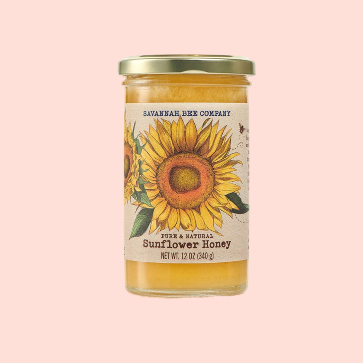 A 12 oz (340 g) jar of Savannah Bee Co. Honey - Sunflower, with vibrant sunflower illustrations, glows against a pink backdrop, showcasing the dedication of beekeepers.