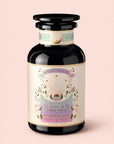 A black glass jar labeled "Tea for Joy: Almond Matcha: Green Matcha Tea with Almonds," featuring pastel floral designs and gold accents, is set against a light pink background. This antioxidant-rich matcha blend delivers a delightful tea experience while naturally supporting metabolism.