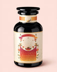 A black glass jar labeled "Tea for Energy: Bohemian Breakfast: Rich Puerh Black Tea Blend" sits on a light pink background. The label is adorned with sun rays, stars, and flowers, evoking a bohemian spirit and highlighting its energizing organic puerh tea blend designed to support energy and digestion.