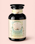 A black jar labeled "Tea for Calm: Mantra Mint: Mint With Rose & Vanilla Herbal Tea," adorned with gold accents, celestial motifs, and botanical illustrations, is set against a light pink background. This organic herbal tea blend features soothing notes of mint, rose, and vanilla, making the Mantra Mint Herbal Tea ideal for moments of tranquility.