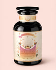 A dark glass jar labeled “Tea for Rest: Venus: Mango Blossom & Nervines Herbal Tea,” adorned with floral designs, gold accents, and a decorative lid, is set against a pale pink background. Infused with an organic mango blossom and nervines herbal blend, this tea is thoughtfully crafted to support relaxation and promote natural collagen production.