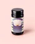 A black canister of “Tea for Intuition: 1111: Pineapple & Butterfly Pea Flower Herbal Tea” with purple and gold details is set against a pale pink background. The label features ingredients such as pineapple, butterfly pea flower, and delicate blue lotus to support your crown chakra connection, and notes the inclusion of plant-silk tea sachets.