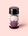 A black tea canister labeled “Tea for Inspiration: Amethyst: Strawberry Passion Fruit Herbal Tea Blend” with organic herbal tea—strawberry passion fruit flavor—featuring a purple and gold design reminiscent of amethyst, set against a pale pink background.