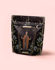 A decorative black pouch featuring "The Emperor: Green Chaga Chai with Lion's Mane and Reishi" artwork—regal figure, floral motifs, and moons—perfect for storing your favorite immune-support mushroom or gunpowder green tea.