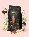 A decorative refill pouch for The Magician - Elderberry-Ginger-Vanilla Herbal Tea features an enchanting mystical design with a robed figure surrounded by flowers, elderberries, ginger, cinnamon sticks, and vanilla pods on a pale pink background. This organic herbal blend is celebrated for its wellness benefits.