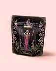 A black resealable pouch shows a woman in a pink dress with a crescent moon headdress, surrounded by pink flowers and stars. At the bottom: "The Queen of Cups: Hibiscus-Vanilla-Berry Tea for Balance & Heart Health.