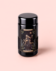 A black jar labeled “The Star: Vanilla-Ginger Beauty Potion with Jasmine & Shatavari” features mystical art of a woman pouring water beneath a starry sky, framed by celestial and floral designs, set against a light pink background—an enchanting vessel inspired by the soothing rituals of organic herbal tea and adaptogenic blends.