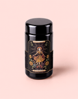 A black tea canister featuring a vibrant label of a woman in a yellow dress surrounded by sunflowers, with “The Sun” and “Tea Abundance” inscribed below, sits against a soft pink background. This eye-catching packaging contains The Sun: Energizing Adaptogenic Herbal Tea with Yaupon, Moringa & Turmeric—an uplifting blend crafted for those seeking both flavor and wellness.
