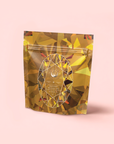 A stand-up pouch with a shiny gold, faceted gemstone design on light pink. The front features a white geometric oval and branding, highlighting Topaz - Caramel Apple Oolong Tea for Optimism & a Lightness of Being.