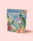 A vibrant package with tropical birds, flowers, and a pyramid on a soft pink background houses Tulum Horchata Chai, an adaptogenic drink featuring gold and blue design accents for a distinctive, eye-catching look.