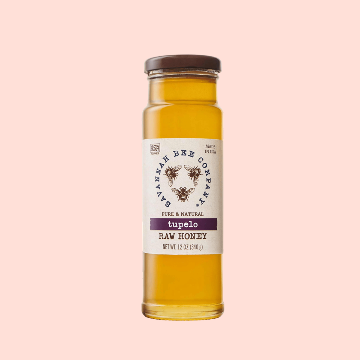 The Savannah Bee Co. Honey - Tupelo is presented in a clear glass bottle with a brown lid and a beige label reading "Savannah Bee Company, Pure & Natural, Made in USA." The 12-ounce (340g) bottle is set against a peach-colored background.