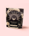 A standing pouch of "Metabolism Balance: Breakfast with Benefits" features an ornate black-and-gold sunburst on light pink—ideal for anyone seeking a metabolism or adaptogen tea to elevate their morning routine.