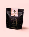 A black, resealable pouch of Magic Hour’s Gypsy Rose Black Tea features gold star patterns, mystical artwork, and a label on a pale pink background, highlighting its biodynamically grown rose tea blend.