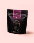 A black resealable pouch labeled "Magic Hour" with gold stars and a purple label reading "Raspberry Earl Grey Black Tea," made with Ceylon black tea and organic freeze-dried raspberries, set against a light pink background.