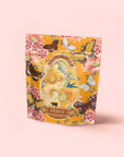 The upright "Venus - Tea for Beauty Sleep" package features a vibrant floral design with an illustrated woman, pink flowers, and butterflies on a yellow background, emphasizing its herbal blend for skin hydration against a pale pink backdrop.