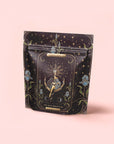 A black and gold resealable pouch adorned with a mystical tarot design labeled "The High Priestess" holds The High Priestess Ginger-Mint-Cardamom Tea: organic, caffeine-free herbal tea for powerful dreams and illuminated insights.