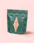 A stand-up pouch with an art deco green and gold geometric pattern, featuring a diamond-shaped beige label reading "Matcha 1111: Highest Grade of Ceremonial Matcha," displayed against a light pink background.