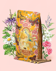 An ornate refill pouch labeled "Venus - Tea for Beauty Sleep" is adorned with illustrations of flowers, butterflies, and herbs on a gentle pink backdrop, with delicate sticks arranged before it. This caffeine-free herbal blend is thoughtfully crafted with beautifying botanicals for an enchanting tea experience.