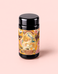A black container with a colorful label featuring floral patterns, insects, and an illustration of a woman’s profile, labeled “Venus - Tea for Beauty Sleep” in gold text, set against a pale pink background. This design hints at an herbal blend specially crafted to promote skin hydration and support collagen production.