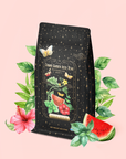 A packet of Watermelon Mint Herbal Iced Tea, featuring floral and watermelon artwork, surrounded by leaves, a watermelon slice, a pink hibiscus flower, and accents of organic peppermint on a pink background. The label reads "Cosmic Garden Iced Teas".