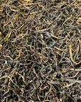A close-up of Yunnan Ancient Tree Black Tea shows loose, dried leaves with dense dark brown and golden yellow strands, sourced from ancient tea trees.