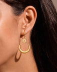 A close-up of a woman's ear wearing Stellar Sisterhood Moonstone Hoops: gold crescent moon earrings with a sun detail and textured finish that catch the light, creating an elegant, celestial-inspired look.