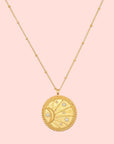 The 18" Sunburst Medallion Necklace features a gold plated round, textured pendant engraved with a crescent moon and white star accents, complemented by delicate bead details along the chain.
