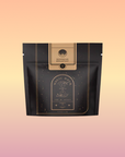 A black and gold resealable pouch labeled "Bohemian Breakfast Black Tea- Probiotic Rich Vanilla Puerh Tea for Digestion & Energy" by Magic Hour, with a celestial design, highlights this organic coffee alternative against a light pink background.