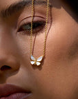 Close-up of a woman's face with smooth skin and natural makeup, holding the Renewed Hope Pearl Butterfly Necklace—delicate 18k gold plated finish—near her eye.