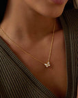 A woman in a ribbed, deep V-neck olive sweater wears the Renewed Hope Pearl Butterfly Necklace—an 18k gold-plated piece featuring a mother of pearl butterfly pendant resting at the base of her neck.