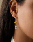 Close-up of a person’s ear wearing the Spiritual Journey Lotus Crystal Earring—an 18k gold plated piece featuring a clear teardrop crystal. Their straight brown hair is tucked back, showcasing this elegant crystal healing jewelry.