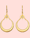 Introducing the Stellar Sisterhood Moonstone Hoops: gold earrings with hammered crescent shapes, sunburst designs, and small white moonstone centers, all elegantly hanging from gold hooks.