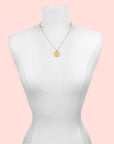The Gold Buddha Pendant Necklace, featuring an 18kt gold plate, is shown on a white dress form mannequin. The pendant rests at chest level against a plain white background.