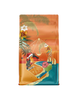 A vibrant, colorful package featuring tropical design elements like palm leaves, flowers, and birds against a gradient background of orange and teal. The front shows a geometric logo with text and graphics, hinting at an Ayurvedic wellness product inside that promises holiday enchantment through mood-enhancing herbs. Lovingly named Hibiscus Holiday Case Packs by Magic Hour.
