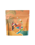 A resealable pouch with a tropical design featuring toucans, palm trees, and a sailboat. It is labeled "Magic Hour" and "Hibiscus Holiday Case Packs" in a geometric diamond shape in the center. Warm sunset colors dominate the background, evoking holiday enchantment blend vibes.