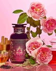 A tea tin labeled “She Rises” sits beside a glass teacup, teapot, cinnamon sticks, loose luxury black tea, and blooming pink roses on a pink background—inviting you to indulge in the radiance-boosting Lakshmi in Abundance: Rose Saffron Black Tea for Good Fortune & Radiance experience.