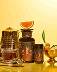 Oshun’s Nectar: Honeyed Herbal Tea for Joy & Radiance is artfully arranged with a teapot, tea cup, glass jar labeled with a fairy and topped with half a grapefruit, a smaller jar, fresh kumquats with leaves, honeycomb, and loose golden honeyed herbal tea on a vibrant yellow background.