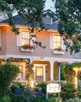 Nestled amid lush greenery and inviting outdoor seating, The Soul of Tea: A Two Day Retreat in Ojai, CA is hosted at a charming two-story inn with beige siding, white trim, vibrant flower boxes, and a glowing porch. A sign nestled in the garden welcomes guests to this tranquil sanctuary—a perfect setting for embracing relaxation and savoring the soulful spirit of tea.