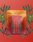 A pouch of Teasoning: Chili Spice Rub, in orange and gold with a magical starry design, sits against a red background surrounded by illustrated green peppers and red onions, highlighting its smoky black tea seasoning.