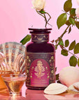 A glass teapot and cup of herbal tea accompany Aphrodite's Alchemy - Damiana & Rose White Tea, white seashells, and a white rose on a pink gradient background—an elegant scene inspired by the goddess of love.