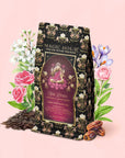 A box of the Monthly Magic Tea Journey Subscription stands in front of illustrated flowers and dates, with loose tea leaves scattered to the left. The packaging features a floral design and a goddess illustration, inviting you to embrace your own Divine Feminine exploration with every cup—a perfect addition to any goddess ritual tea collection.