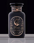 A dark blue bottle labeled "Astrology Bundle: Capricorn, Aquarius, Pisces" with a crescent moon, stars, and a fish design. The label includes floral accents and a celestial motif, evoking the elegance of Magic Hour. The bottle stands on a reflective surface against a dark background.